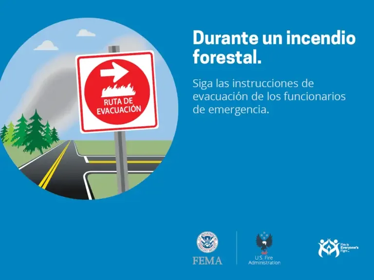 Un cartel de señalización vial advierte sobre la importancia de seguir la ruta de evacuación durante un incendio forestal, con un paisaje de fondo que incluye árboles y montañas.